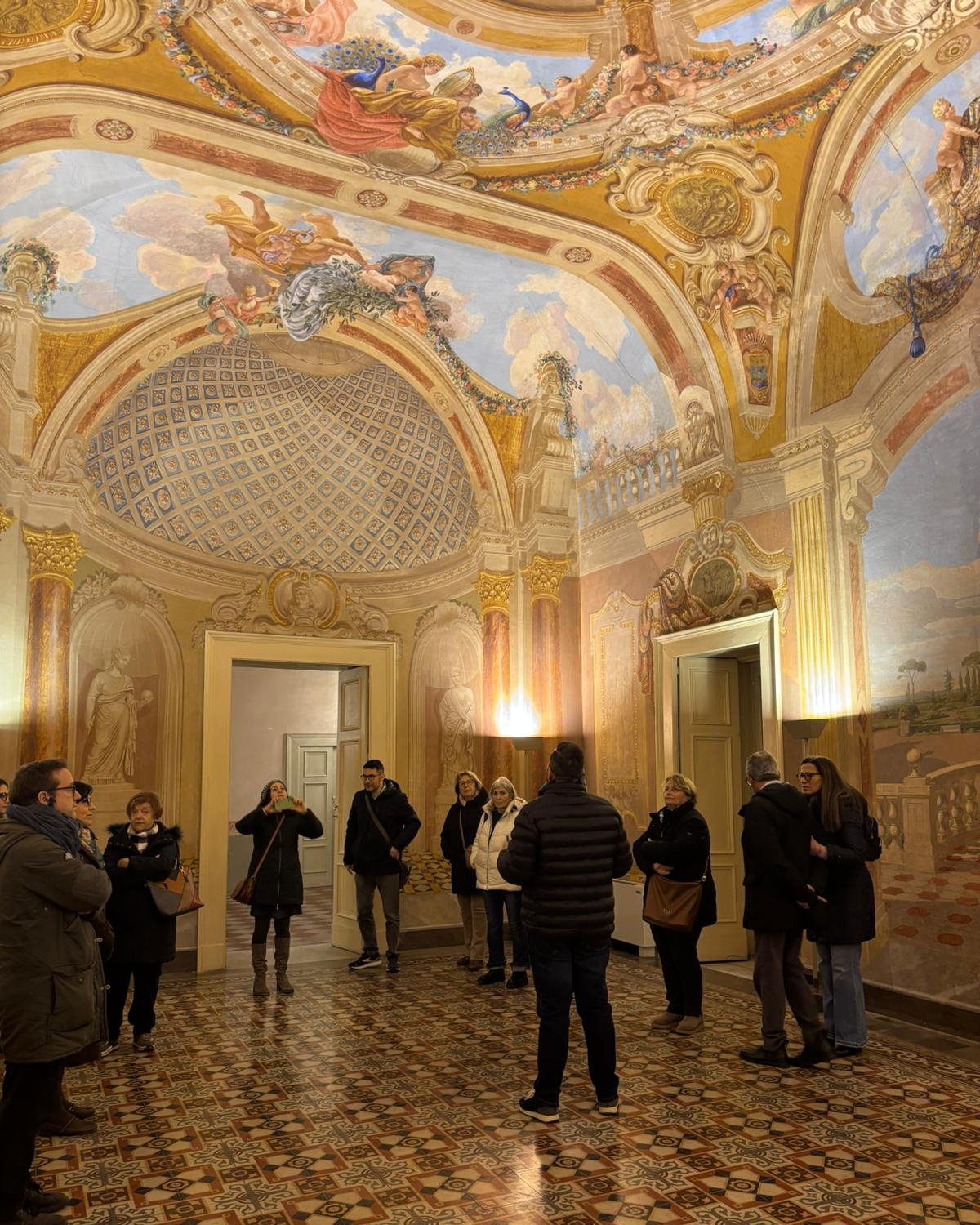 Gruppo di visitatori durante una visita guidata in una sala affrescata di un palazzo storico