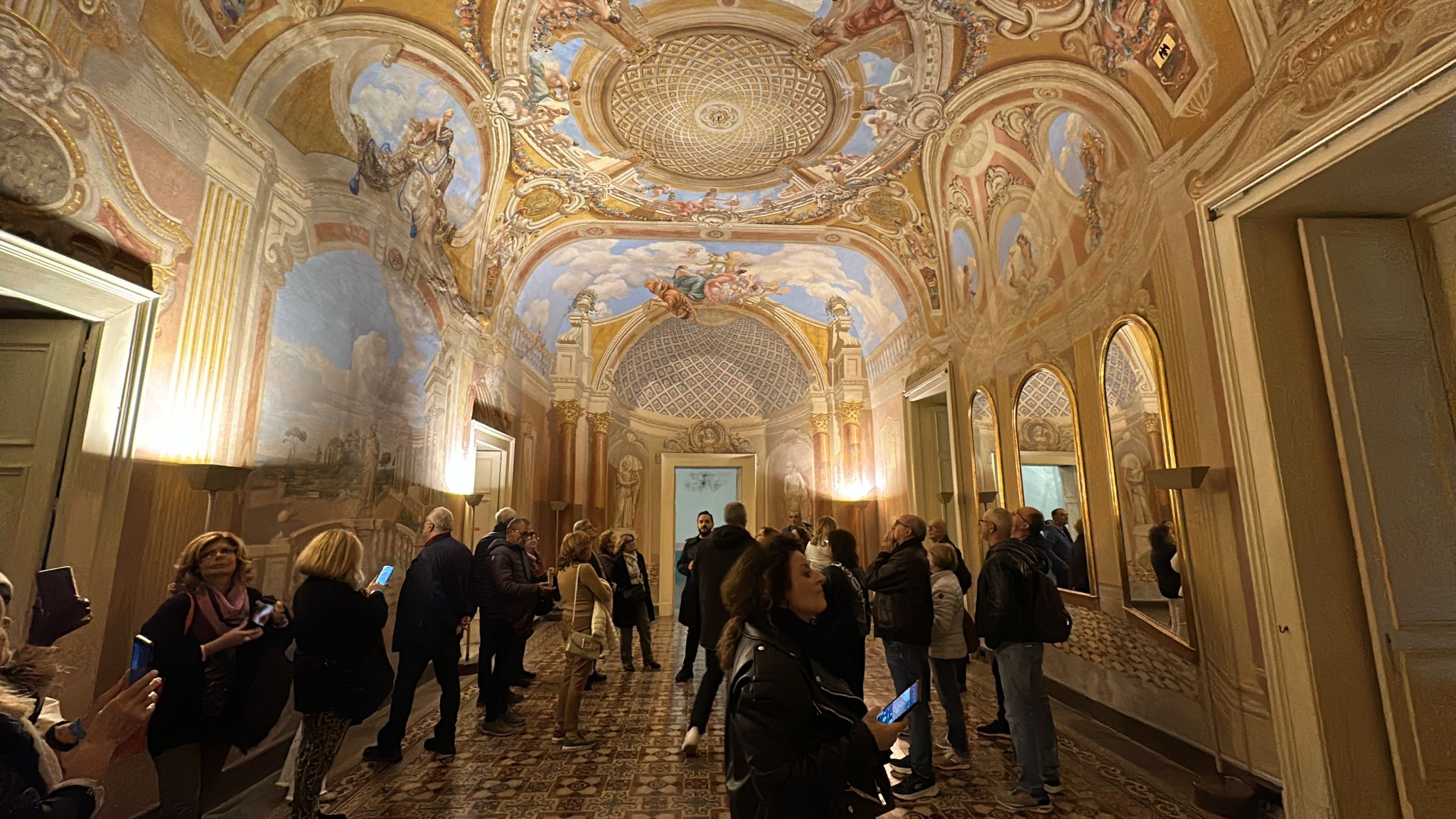 Visitatori riuniti in una grande sala affrescata durante un itinerario guidato